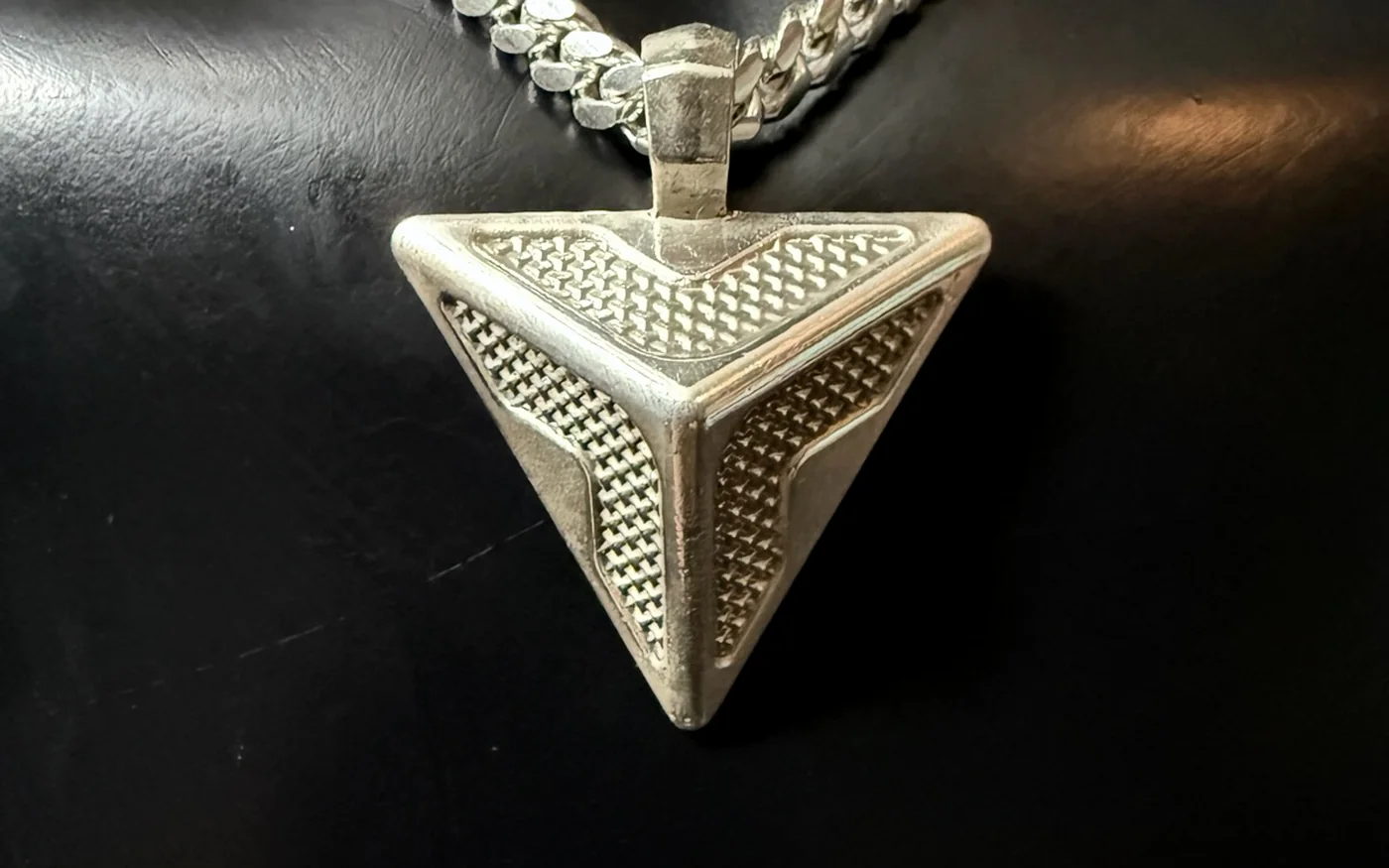 The Triangle Pendant lying on black leather with its heavy silver chain